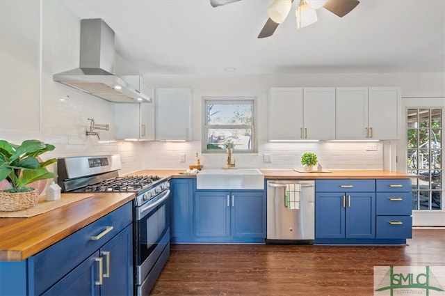 kitchen with butcher block countertops, white cabinetry, stainless steel appliances, and wall chimney range hood