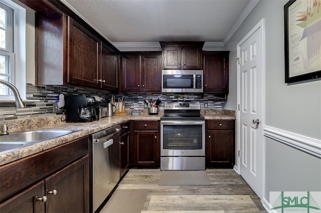 kitchen with dark brown cabinetry, sink, stainless steel appliances, light hardwood / wood-style floors, and ornamental molding