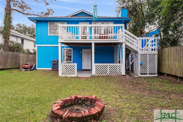 rear view of house featuring a lawn, a wooden deck, and an outdoor fire pit