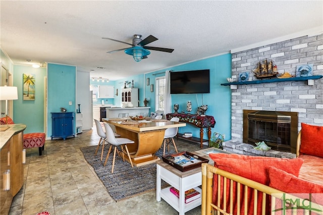 living room featuring ceiling fan, a fireplace, crown molding, and a textured ceiling