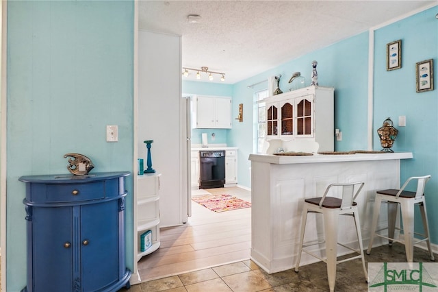 kitchen featuring kitchen peninsula, a kitchen breakfast bar, a textured ceiling, dishwasher, and white cabinets