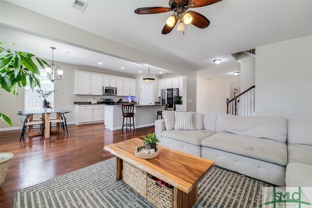 living room featuring ceiling fan with notable chandelier and dark wood-type flooring