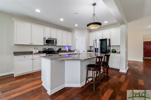 kitchen with dark hardwood / wood-style flooring, stainless steel appliances, white cabinetry, and a center island with sink