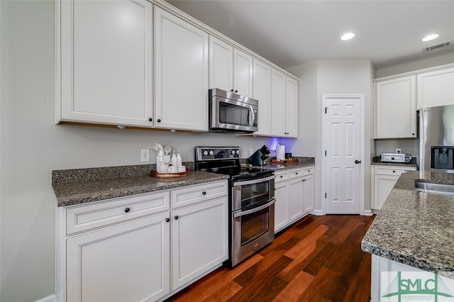 kitchen with stainless steel appliances, white cabinetry, dark wood-type flooring, and dark stone countertops