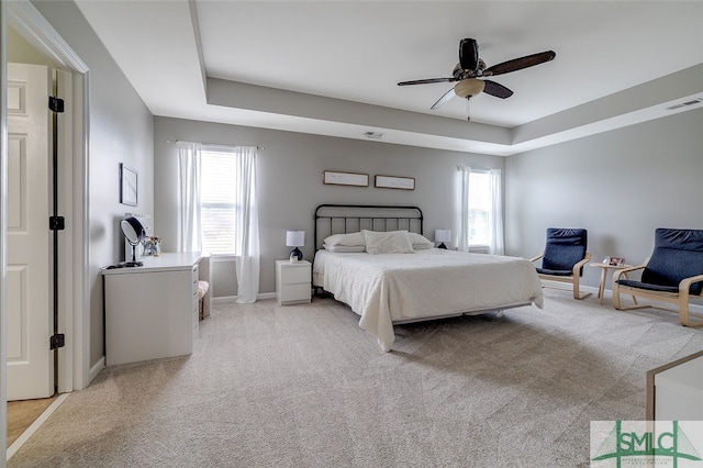 bedroom with ceiling fan, light carpet, and a tray ceiling