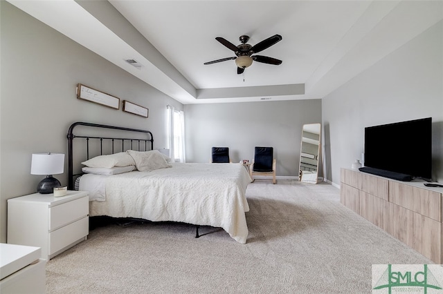 bedroom featuring a raised ceiling, ceiling fan, and light carpet