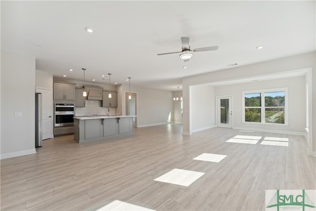 unfurnished living room featuring ceiling fan with notable chandelier, light hardwood / wood-style flooring, and sink