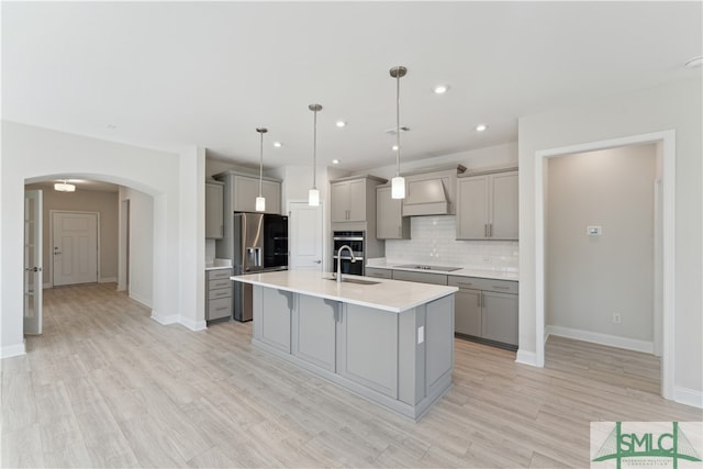 kitchen featuring premium range hood, light hardwood / wood-style floors, a kitchen island with sink, pendant lighting, and gray cabinets