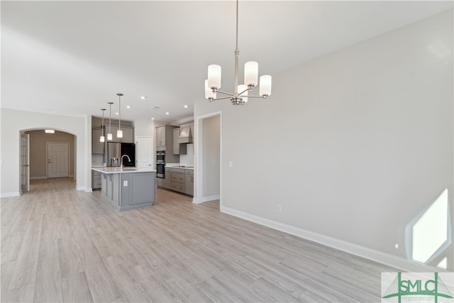 kitchen featuring pendant lighting, light hardwood / wood-style floors, appliances with stainless steel finishes, and an island with sink