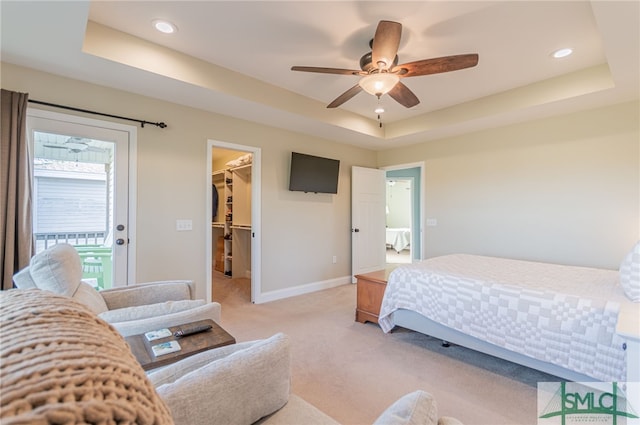 bedroom with a raised ceiling, a walk in closet, ceiling fan, light colored carpet, and a closet