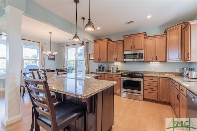 kitchen featuring appliances with stainless steel finishes, pendant lighting, light hardwood / wood-style flooring, a center island, and a breakfast bar area