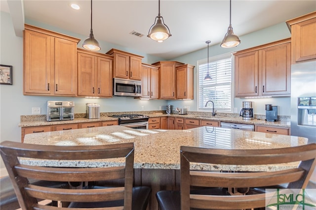 kitchen with a kitchen bar, sink, pendant lighting, and appliances with stainless steel finishes