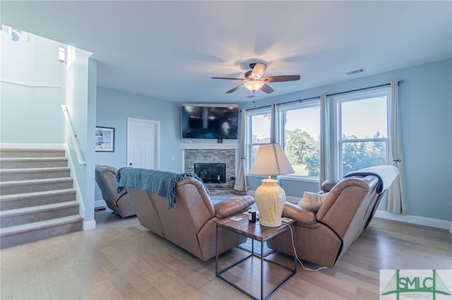 living room featuring light hardwood / wood-style flooring, ceiling fan, and a stone fireplace