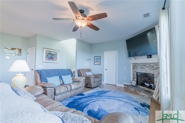 living room featuring hardwood / wood-style floors, ceiling fan, and a stone fireplace