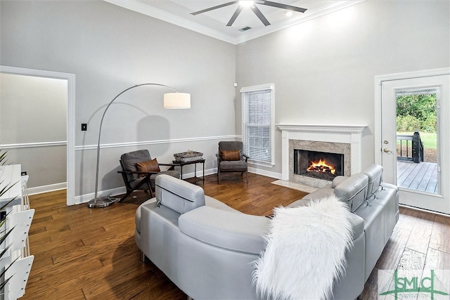 living room with a high end fireplace, ornamental molding, ceiling fan, dark wood-type flooring, and a high ceiling