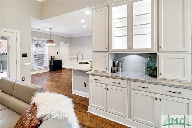 kitchen with light stone countertops, crown molding, dark wood-type flooring, sink, and white cabinets