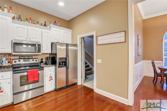 kitchen featuring appliances with stainless steel finishes, dark stone counters, ornamental molding, hardwood / wood-style flooring, and white cabinetry