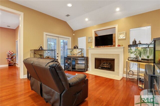 living room featuring hardwood / wood-style floors, vaulted ceiling, and a tiled fireplace