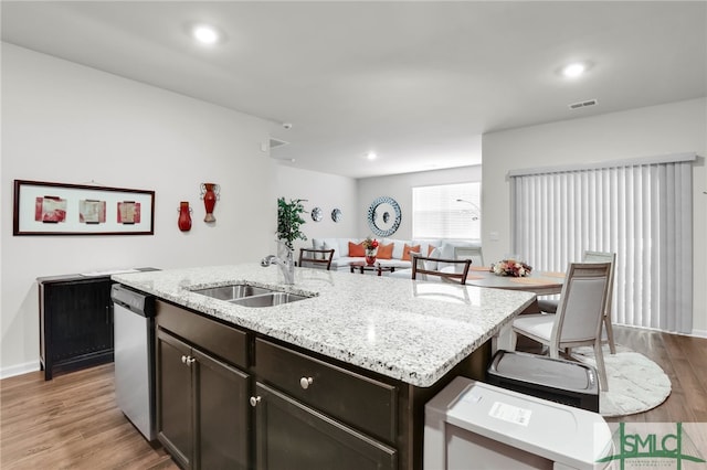 kitchen with dishwasher, sink, light hardwood / wood-style floors, dark brown cabinets, and a center island with sink