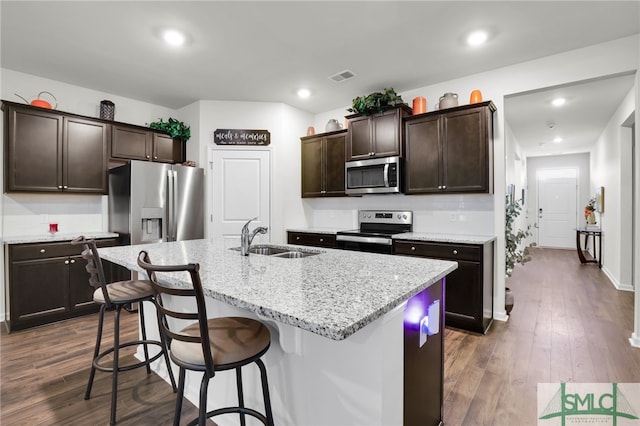 kitchen with sink, an island with sink, appliances with stainless steel finishes, dark brown cabinets, and dark hardwood / wood-style flooring