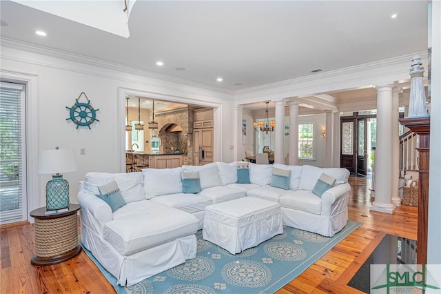 living room with a chandelier, wood-type flooring, decorative columns, and crown molding