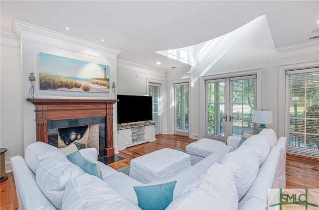 living room featuring light hardwood / wood-style floors, ornamental molding, a tile fireplace, and french doors