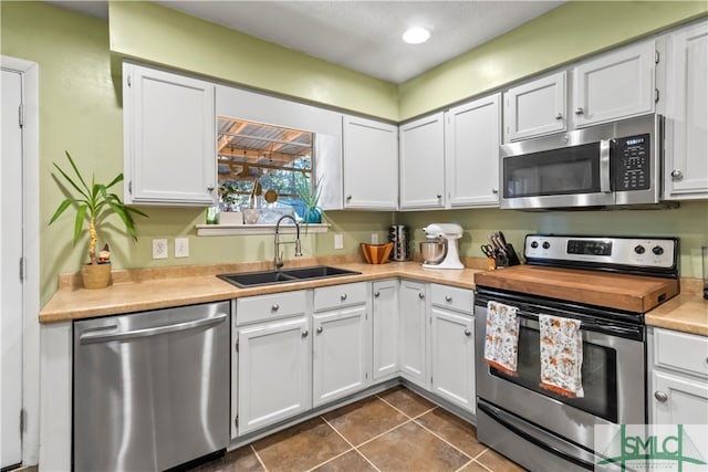 kitchen with stainless steel appliances, white cabinetry, dark tile patterned floors, and sink