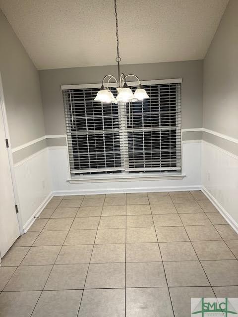 unfurnished dining area with a notable chandelier, light tile patterned floors, and a textured ceiling