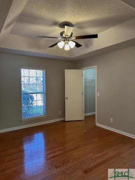 empty room with a tray ceiling, a textured ceiling, dark hardwood / wood-style floors, and ceiling fan