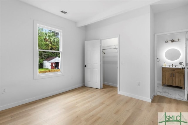 unfurnished bedroom with connected bathroom, a spacious closet, and light wood-type flooring