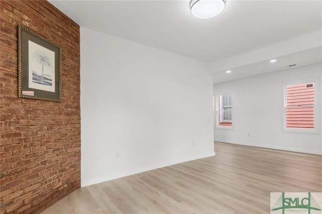 unfurnished room featuring brick wall and light wood-type flooring