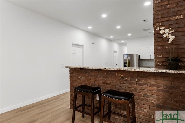 bar with stainless steel fridge with ice dispenser, light hardwood / wood-style floors, white cabinetry, and light stone counters