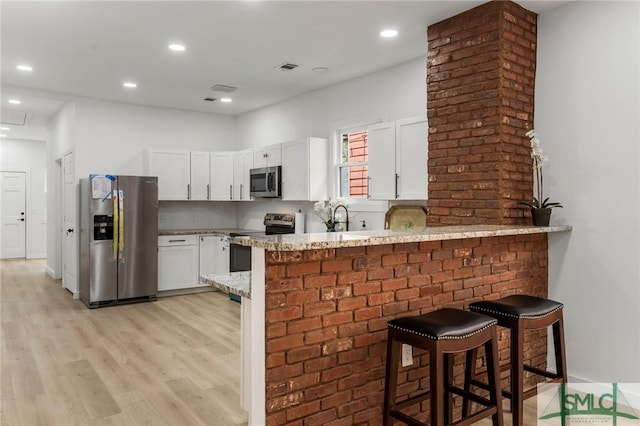 kitchen featuring kitchen peninsula, a breakfast bar, stainless steel appliances, sink, and white cabinets