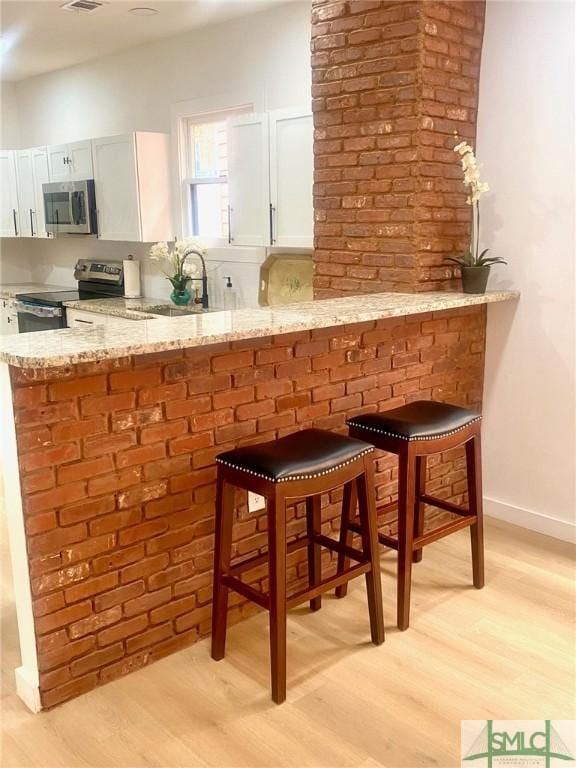 interior space featuring white cabinets, a breakfast bar, light stone counters, and stainless steel appliances