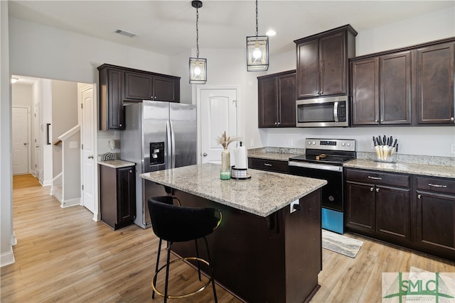 kitchen featuring appliances with stainless steel finishes, a breakfast bar, a kitchen island, dark brown cabinets, and light wood-type flooring