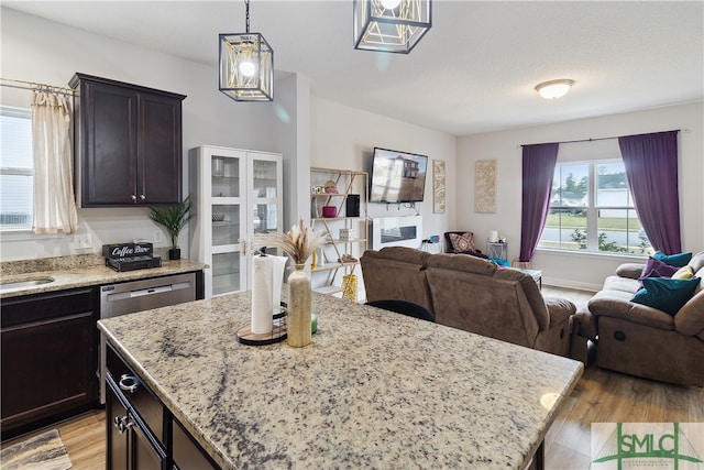 kitchen featuring a center island, decorative light fixtures, light wood-type flooring, dark brown cabinets, and light stone counters