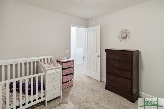 bedroom with a crib, a textured ceiling, and light carpet