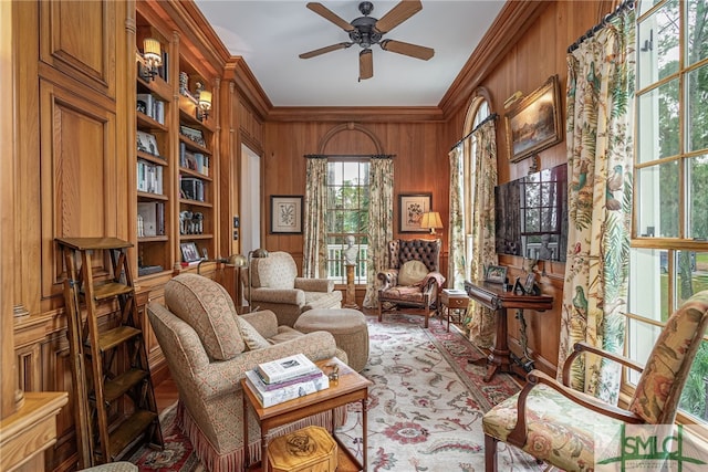 living area with ceiling fan, wood walls, and crown molding