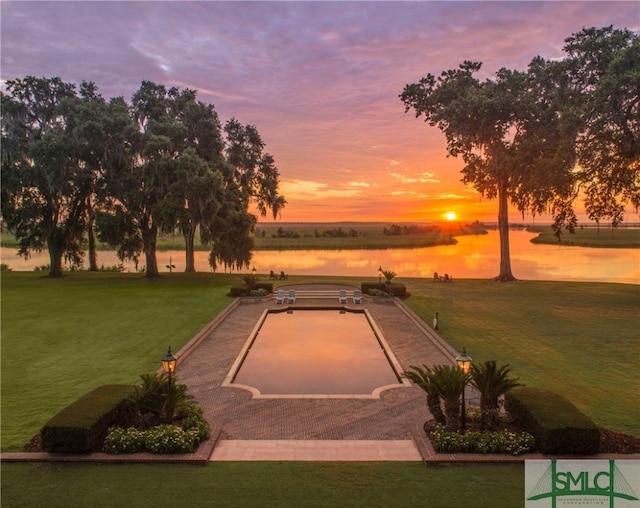 pool at dusk featuring a lawn and a water view