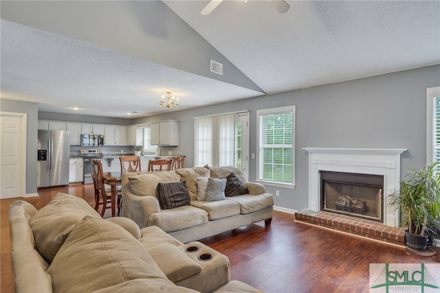 living room featuring vaulted ceiling, a brick fireplace, ceiling fan, a textured ceiling, and dark hardwood / wood-style flooring