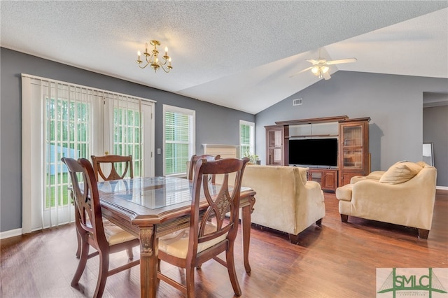 dining area featuring ceiling fan with notable chandelier, wood-type flooring, a textured ceiling, and vaulted ceiling