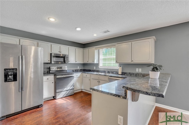 kitchen with kitchen peninsula, a textured ceiling, appliances with stainless steel finishes, dark hardwood / wood-style flooring, and white cabinetry