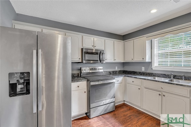 kitchen with appliances with stainless steel finishes, a textured ceiling, dark wood-type flooring, sink, and white cabinets