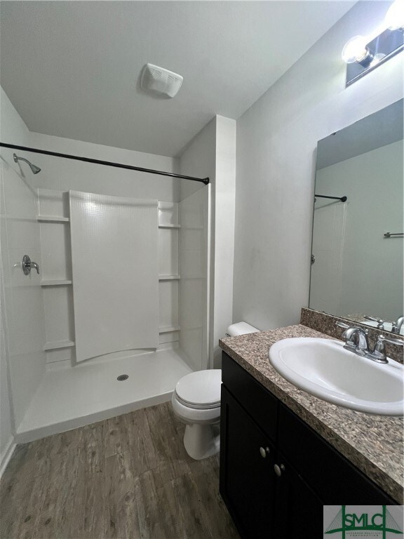 bathroom with a shower, wood-type flooring, vanity, and toilet