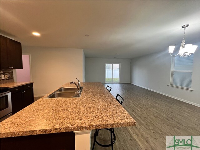 kitchen with a breakfast bar, dark wood-type flooring, an inviting chandelier, sink, and an island with sink