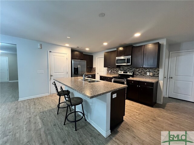 kitchen featuring sink, an island with sink, a breakfast bar, appliances with stainless steel finishes, and light wood-type flooring