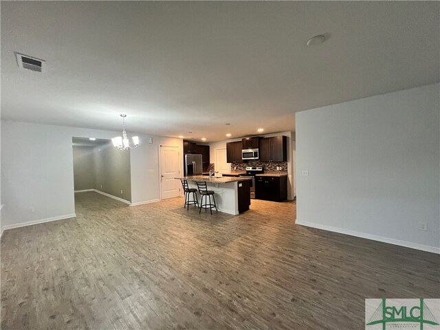 kitchen featuring backsplash, a center island with sink, dark hardwood / wood-style floors, appliances with stainless steel finishes, and a breakfast bar area