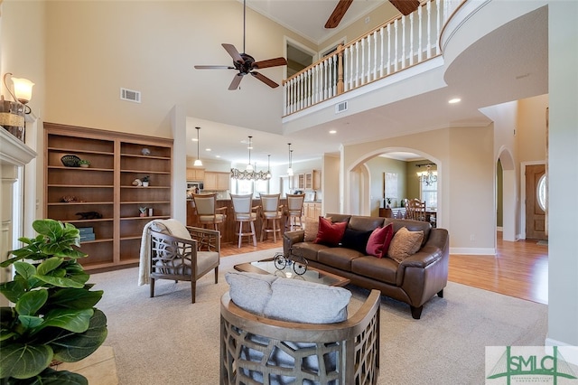 living room with light hardwood / wood-style flooring, ceiling fan with notable chandelier, a high ceiling, and ornamental molding