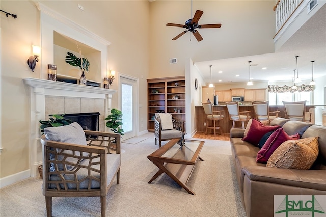 living room with light carpet, a high ceiling, ceiling fan with notable chandelier, and a tiled fireplace