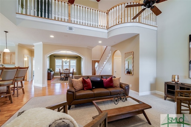 living room featuring ceiling fan with notable chandelier, crown molding, a high ceiling, and light hardwood / wood-style flooring